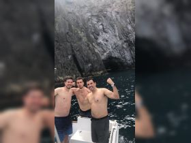 Three friends pose for a fun photo on a boat near dramatic cliffs, capturing the excitement of their ocean adventure.