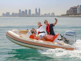 A couple enjoys a fun moment taking a selfie on a speedboat with a stunning city skyline in the background, capturing the excitement of their water adventure.