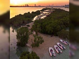 A stunning sunset view over a mangrove island, with a group of people exploring the shoreline and several boats anchored nearby — perfect for eco tours and nature adventures.