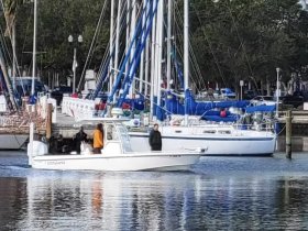 A small boat navigates through a marina, showcasing the vibrant atmosphere of boating life with other vessels in the background.