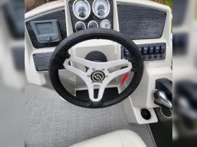 A close-up view of a boat's helm featuring a sleek steering wheel and control panel, showcasing the modern design and functionality of the vessel's interior.
