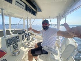 A cheerful captain gives a thumbs up from the helm of a boat, showcasing the control console and a beautiful water view — perfect for a day on the water.