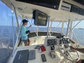 A young boy stands at the helm of a boat, observing the water while an adult operates the controls. This interior shot captures the essence of navigating on the water.