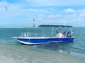A vibrant blue pontoon boat docked near a sandy shore, with a lighthouse in the background, perfect for day trips and coastal adventures.