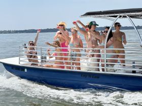 A lively group of friends celebrates aboard a pontoon boat, enjoying drinks and sunshine on the water — perfect for summer parties and fun outings.
