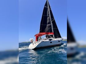A sleek sailboat navigates through vibrant blue waters, showcasing its impressive black sails and red canopy — perfect for adventurous sailing trips.