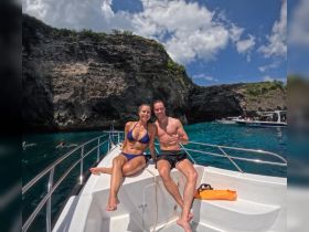A happy couple poses on the bow of a boat, enjoying a sunny day surrounded by stunning cliffs and clear waters — perfect for a memorable adventure.