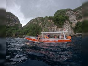 A lively group enjoys snorkeling and swimming around a boat during an island-hopping adventure, surrounded by stunning coastal cliffs.