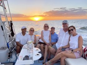 A cheerful group enjoys a sunset cruise on the water, capturing a perfect moment of camaraderie and celebration with drinks in hand.