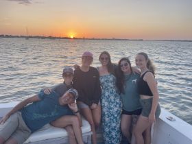 A cheerful group of friends poses for a photo on a boat at sunset, capturing the essence of a perfect evening on the water.