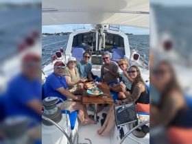 A cheerful group enjoys a meal aboard a sailboat, showcasing the perfect blend of good company and sailing adventure on the water.