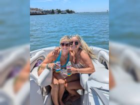Two friends enjoy a sunny day on a pontoon boat, celebrating with drinks and smiles — perfect for summer outings and fun on the water.