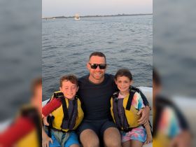 A joyful moment captured with a father and his two children on a boat, all wearing life jackets and enjoying their time on the water.