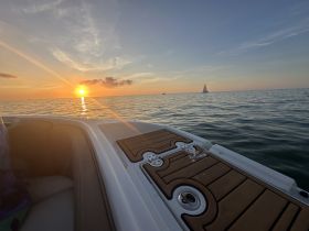 A serene sunset view from the deck of a boat, showcasing the tranquil sea and distant sailboats — perfect for evening cruises.