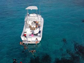 A lively group enjoys snorkeling around a boat in crystal-clear waters, making for a perfect family adventure on the water.