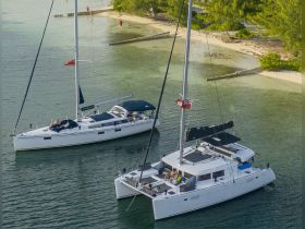 Two catamarans anchored in serene waters, with guests relaxing on deck, showcasing the perfect setting for a beach getaway or sailing adventure.