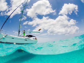 A thrilling moment captured as a person jumps from a sailboat into the crystal-clear waters, showcasing the excitement of a sailing adventure.