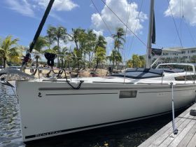 A sleek Beneteau yacht docked in a serene marina, surrounded by palm trees and clear blue skies — perfect for a day of sailing or relaxation.