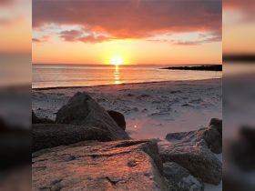 A stunning sunset over a tranquil beach, with the sun reflecting on the calm waters — a perfect scene for relaxation and coastal beauty.