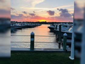 A picturesque sunset over a marina filled with boats, creating a serene atmosphere perfect for evening strolls or romantic getaways.