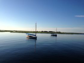 Two sailboats peacefully anchored in calm waters, surrounded by lush greenery — a serene scene perfect for sailing enthusiasts.