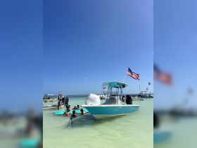 A lively group enjoys a fun day at the beach, relaxing and swimming around a boat in shallow waters — perfect for summer adventures and family outings.