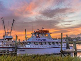 A stunning sunset view of the 'Navigator' yacht docked at the marina, showcasing its elegant design against a colorful sky.
