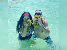 A playful couple poses in the clear waters, holding seaweed and enjoying their time together — a fun moment captured during a tropical adventure.