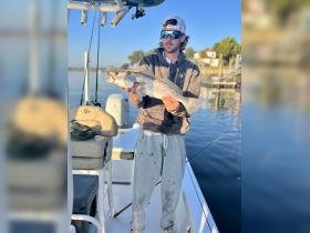 A fisherman proudly displays his catch aboard a boat, showcasing the thrill of fishing on the water.