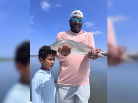 A proud moment as a man and a child display a freshly caught fish, showcasing the joy of fishing together on the water.
