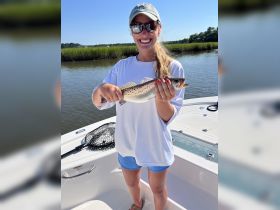 A joyful woman proudly displays her catch while fishing from a boat, showcasing the thrill of a successful day on the water.