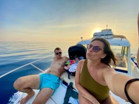 A couple enjoys a serene sunset on a boat, capturing a memorable moment with their baby — perfect for family outings on the water.