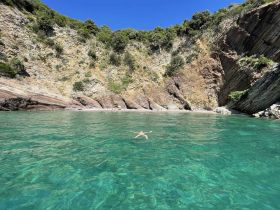 A serene view of a swimmer enjoying the crystal-clear waters near a stunning rocky coastline, perfect for beach lovers and adventure seekers.