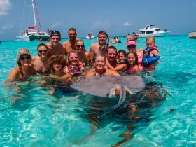 A joyful group of people interacts with a stingray in shallow, clear waters, creating a memorable wildlife experience perfect for family adventures.