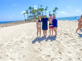A cheerful group poses together on a beautiful beach, surrounded by palm trees and clear blue waters — perfect for memorable vacation moments.