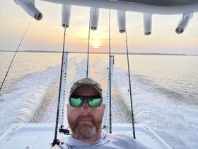 A fisherman captures a selfie on a boat during a stunning sunset, showcasing the serene beauty of a fishing trip on the water.