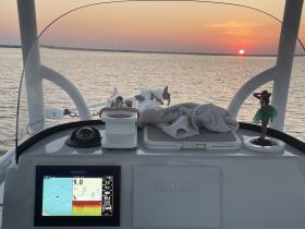 A serene view from the helm of a boat, showcasing the console and a beautiful sunset over the water — perfect for navigating evening cruises.