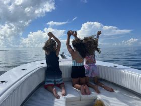 A joyful moment captured as three children celebrate on the deck of a boat, enjoying a beautiful day on the ocean under a bright blue sky.
