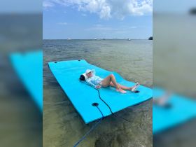A woman relaxes on a floating mat in clear waters, enjoying a sunny day — perfect for summer fun and water activities.