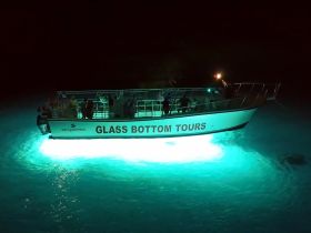 A glass bottom boat tour at night, illuminated by vibrant lights, showcasing an exciting ocean experience with guests onboard.