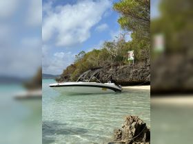 A sleek speedboat is docked on a sandy beach, surrounded by clear turquoise waters and lush greenery, perfect for a day of relaxation and adventure.