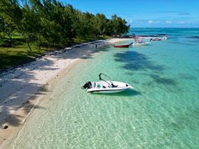 A stunning aerial view of a speedboat docked on a sandy beach, surrounded by crystal-clear waters and lush greenery, perfect for a day of relaxation and exploration.