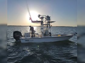 A fisherman prepares for a day on the water aboard a Pathfinder boat, with a stunning sunset backdrop creating a perfect fishing atmosphere.
