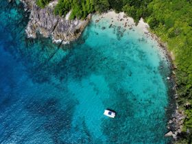 A stunning aerial view of a boat anchored in crystal-clear turquoise waters, surrounded by lush greenery and rocky shores — a perfect representation of tropical paradise.