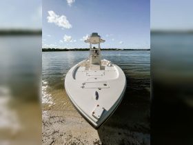 A sleek speedboat is docked on the shore, showcasing its front profile against a clear blue sky — perfect for water adventures and fishing trips.