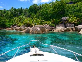 A stunning view from the bow of a boat cruising through crystal-clear turquoise waters, surrounded by lush greenery and rocky coastline — an ideal scene for island exploration.