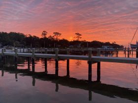 A serene sunset view reflecting on calm waters, with a dock and silhouettes of trees in the background. Perfect for capturing the tranquility of waterfront locations.