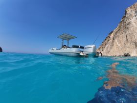 A sleek speedboat is anchored in crystal-clear turquoise waters, showcasing its design against a stunning rocky backdrop — perfect for day trips and water adventures.