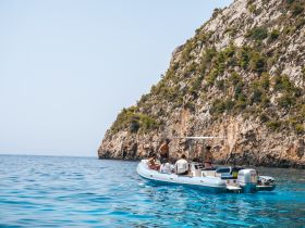 A group enjoys a sunny day on a boat near a stunning coastline, perfect for summer adventures and exploring the beautiful waters.