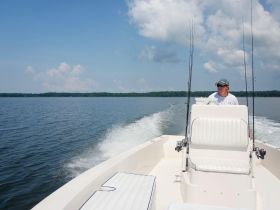 A man navigates a fishing boat on calm waters, showcasing the thrill of outdoor fishing adventures.
